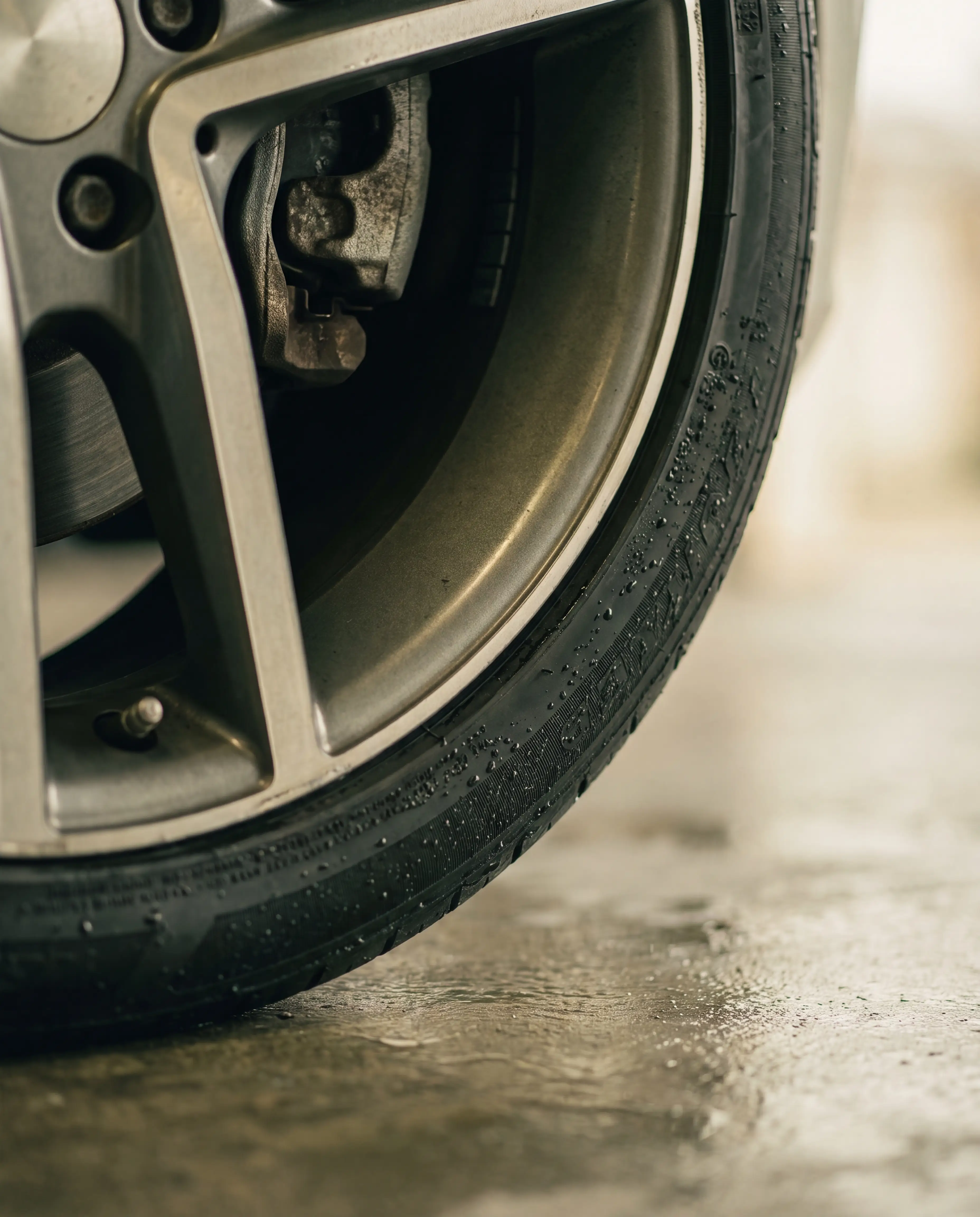 Close detail of a car's alloy wheel, brake caliper and tyre on wet ground.